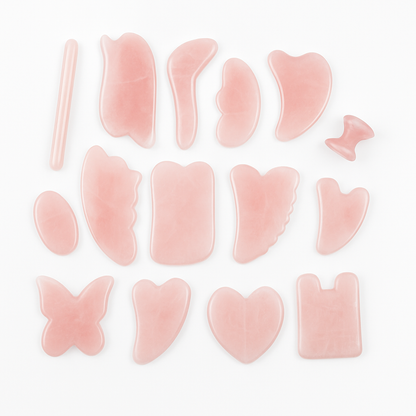 A collection of rose quartz Gua Sha tools in various shapes including heart, butterfly, and leaf, used for facial massage and skin care.